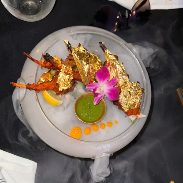 Gold-leafed chicken lollipops with green chutney and an orchid, served on a smoky platter.
