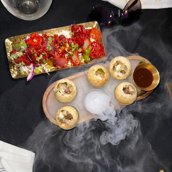 Pani Puri with smoke and a red appetizer on a golden tray, with sunglasses and a glass.