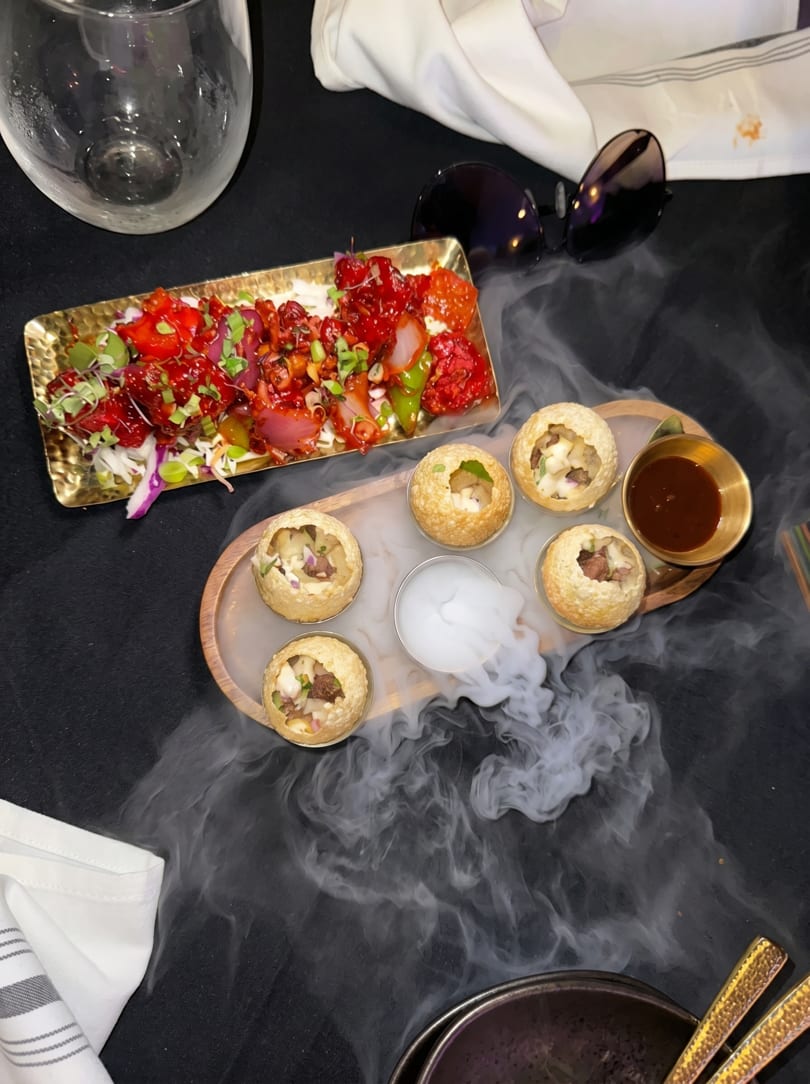 Pani Puri with smoke and a red appetizer on a golden tray, with sunglasses and a glass.