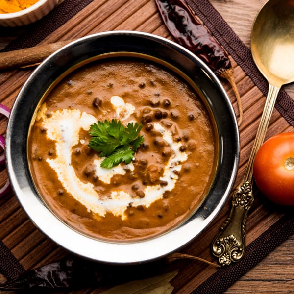 Overhead view of a bowl of creamy Indian Dal Makhani garnished with cilantro and cream, surrounded by spices.